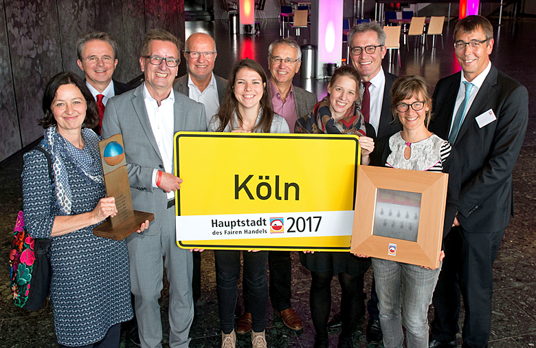 Eine Gruppe, die das Ortsnamensschild Köln trägt, lächelt in die Kamera.